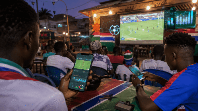 Football betting in The Gambia with fans using mobile betting apps while watching live football matches.